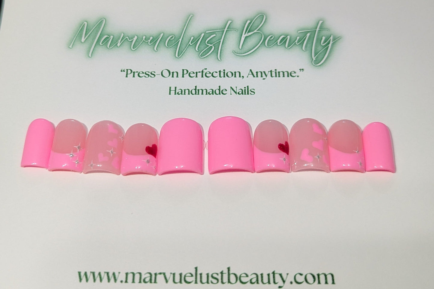 Soft pink press-on nails with decorative elements on a white background, featuring 'Marvuelust Beauty' branding.