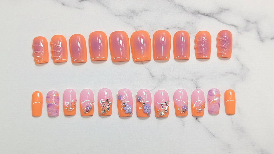 Row of orange and pink gradient nails with floral designs on a light gray background