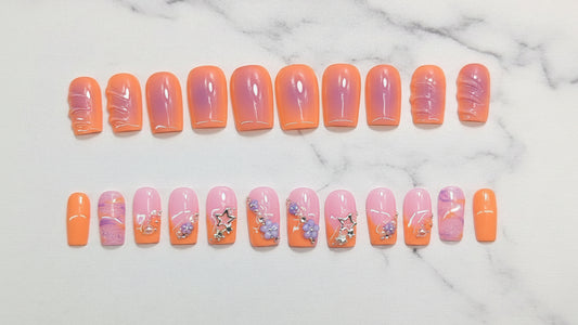 Row of orange and pink gradient nails with floral designs on a light gray background